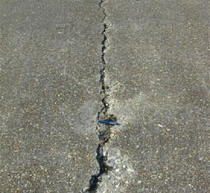 Close-up photo of a single medium-severity crack in a PCC slab. The crack appears to be 1/2 in (13 mm) wide           and shows areas of spalling.